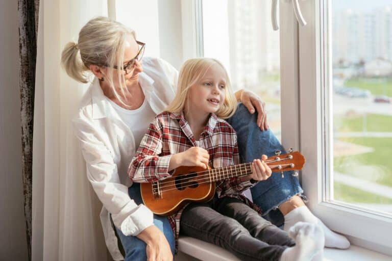Woman and daughter playing ukelele at window